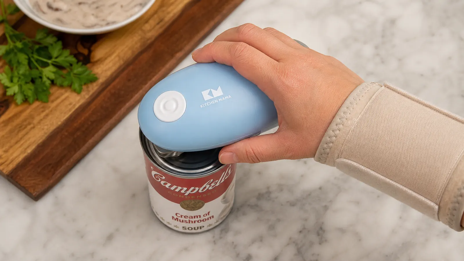 A hand with a wrist brace pressing an automatic electric can opener onto the top of a can, opener clamped and rotating