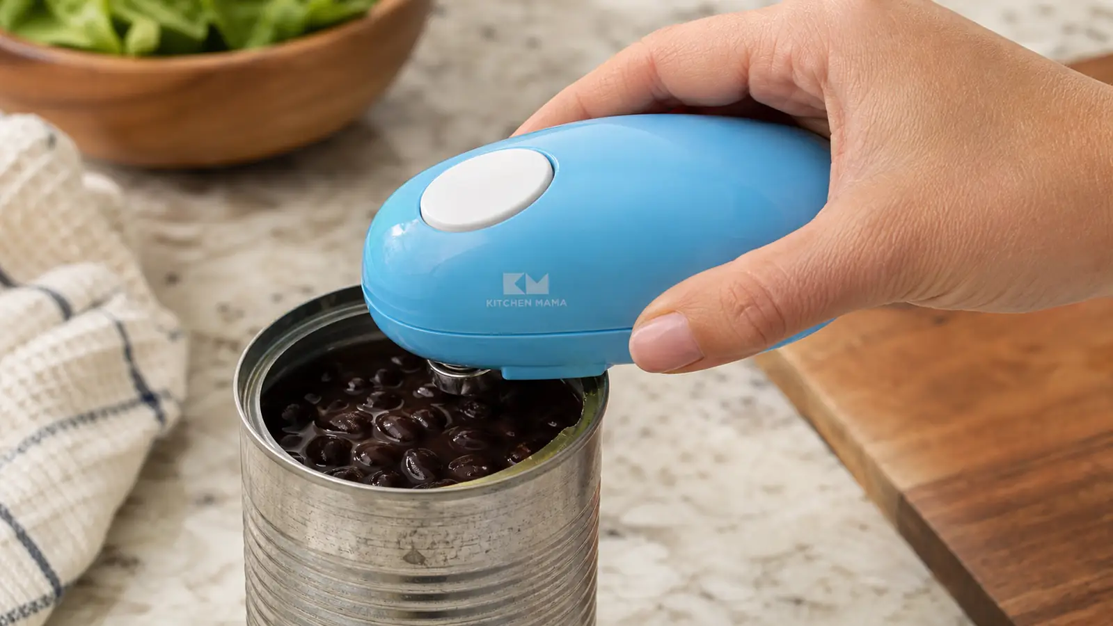 A hand clamping the automatic electric can opener onto the rim of a can of black beans on a counter